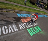 A photo of a bicyclist riding along a paved surface with painted lettering on it.