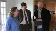 Photo of three people standing and talking to each other inside a home: two men and a woman.