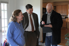 A photo of three people standing and talking to each other, two men and a woman, inside a home.