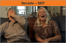 Photo of a man and woman sitting on a couch next to each other, facing the camera and laughing uproariously.