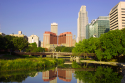 Photo of tall buildings in a city skyline, with a river spread out in the foreground.