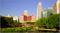 Photo of tall buildings in a city skyline, with a river spread out in the foreground.