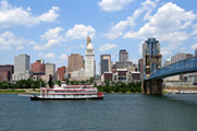 Photo of a busy city skyline with a river in the foreground and a large boat on it.