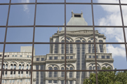Photo of a large, historic-looking downtown building reflected in the glass of the building across the street.