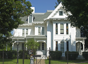 Photo of a large white home with a wrought iron fence in front of it.