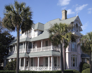 Photo of a large, ornate, Southern home, with sprawling porches on both the first and second levels and palm trees standing nearby.