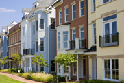 Photo of a block of close-knit townhomes or condos in varying styles and paint colors, on a sunny day.