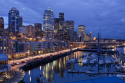 Photo of a city skyline at night, with a cluster of lit-up office buildings on the the left and a river stretching out beside them.