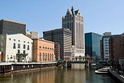 Photo of a cluster of inner-city buildings, with a river flowing in the foreground.
