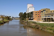Photo of a riverfront with buildings on the right side and a stretch of grass on the left.
