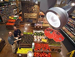 Photo of NREL Senior Engineer Michael Deru measuring light levels in the produce department of a Whole Foods Market as Kyle Maier, Whole Foods Produce Team Leader, looks on.