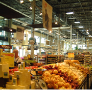 Image shows a well-lit, warehouse-like produce section of a Whole Foods store. Much of the lighting in the photo eminates from windows along the left side of the photo.
