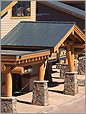 Photo of a building with an angled black roof supported by wood and stone columns. 