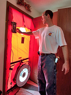 Photo of a man standing in front of a door performing a blower door test.
