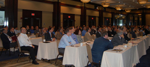 Photo of a conference room with people seated side by side at rows of tables.