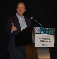 Photo of a man standing at a podium, talking into a microphone.
