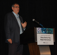 Photo of a man standing at a podium, talking into a microphone.
