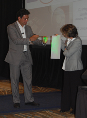 Photo of a man and a woman standing. The woman is holding a piece of paper, and the man is shining an LED light on the paper to create a green glow.