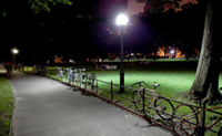 Photo of a post-top outdoor light along a walkway through a wooded park.