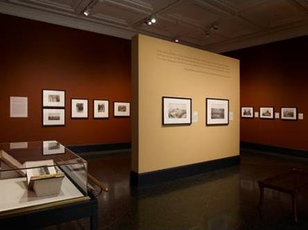 Photo of museum exhibit with pictures hanging on walls and illuminated by track lights.