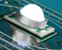 Photo of an LED light: a white dome with a round silver collar on a flat square substrate, which is on a circuit board