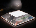 Photo of what looks like a transparent three-dimensional pyramid containing compartments with the top sliced off, the top remaining part being a white rectangle. There appears to be a person's finger above it.