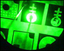 Photo of a microscope image of a mini deep green LED. Image shows part of a circle with intersecting green bands, green and black shapes, and a smaller glowing circle at the center.