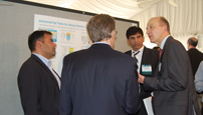 Photo of four men talking in front of a poster.