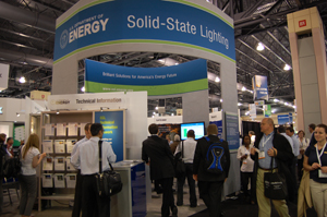Photo of DOE SSL exhibit booth, with LIGHTFAIR attendees and staff standing around and inside the booth and attendees walking around the booth.
