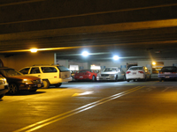 Photo at night of a parking garage filled with cars, with bright lights overhead.