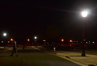 Photo of a street at night with a post-top street light in the right foreground and two more in the background.