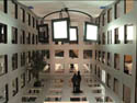 Image of two people standing in a modernistic room with walls and floor composed of a grid of transparent glass rectangles, and glowing rectangles hanging from the ceiling.