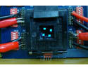 Photo of a dark blue square on a circuit board, with four tiny light blue lights lit within the square. Wires connect on both the right and left.