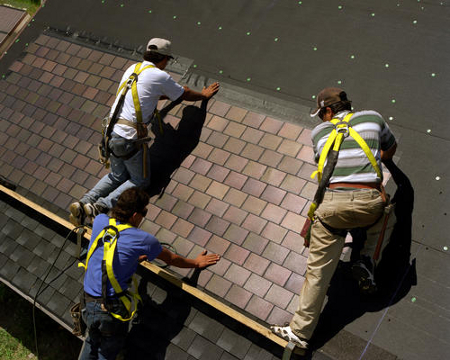 Photograph of three men placing solar tiles on a roof.