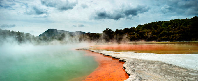 Photo of an expanse of land and water producing geothermal energy, with steam rising from the water, and mountains in the background.