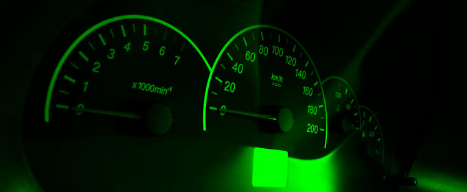 Photo of a vehicle speedometer, along with an odometer, with glowing green readout against a dark background.