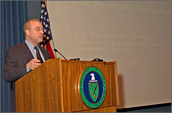 John Mizroch, EERE Principal Deputy Assistant Secretary, stands behind a podium in front of a large projection screen. Information about DOE's Renewable Energy Forum is displayed on the screen.