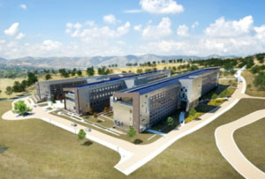 Aerial photo of a large building nestled in front of a green foothill. The building has two large wings and many large windows for optimal daylighting and temperature control.