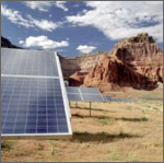 Photo of photovoltaic arrays in front of a red mountain with a blue sky backdrop.