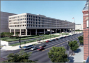 Photo of a long, brown office building standing in front of a street with several cars stopped at a traffic building.