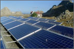 Photo of numerous PV arrays aligned in a mountainous region with a house in the background and a bird flying overhead.