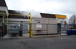 Photo of a fenced-in fuel cell system in front of a building with steam rising in the background.