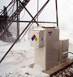 Photo of a fuel cell system in front of a radio tower with snow on the ground.