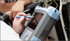 Photo of a person holding a handheld measuring device with their right hand. With their left hand they are holding a stylus pen that is placed on top of a small glass screen.