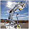 Photo of a large mechanical device, like a mechanical arm, standing outside against a sunny blue sky.