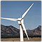 Photo of a wind turbine against a clear blue sky, with a mountain range in the distance.