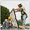 Photo of two men in hard hats.  One is carrying a large white panel.