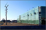 Photo of a glass-fronted building with solar panels in front of the building and wind turbines on the roof.