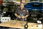 Photo of a man standing in a garage. Two cars are parked behind him. In front of him is a table that has a variety of car parts on top of it, including hoses, a fuel pump, a fuel gauge, a fuel rail, and other assorted parts. Photo links to Alternative Fuels and Advanced Vehicles Data Center, Alternative and Advanced Vehicles Web site.