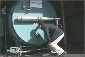 Photo of a large cylindrical machine.  A man crouches in front of it, inspecting it.  Photo links to the Industrial Technologies Program, Super Boiler Overview.